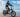 A rider cruising on a sleek black WILDEWAY FW11 folding fat-tire electric bike across a sunny, soft sandy beach next to the ocean waves.