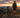 A matte black Wildeway WANDER Max e-bike parked on a scenic ridge overlooking a vast forest at sunset , with its LCD screen clearly visible in the foreground brightly displaying a full battery icon.